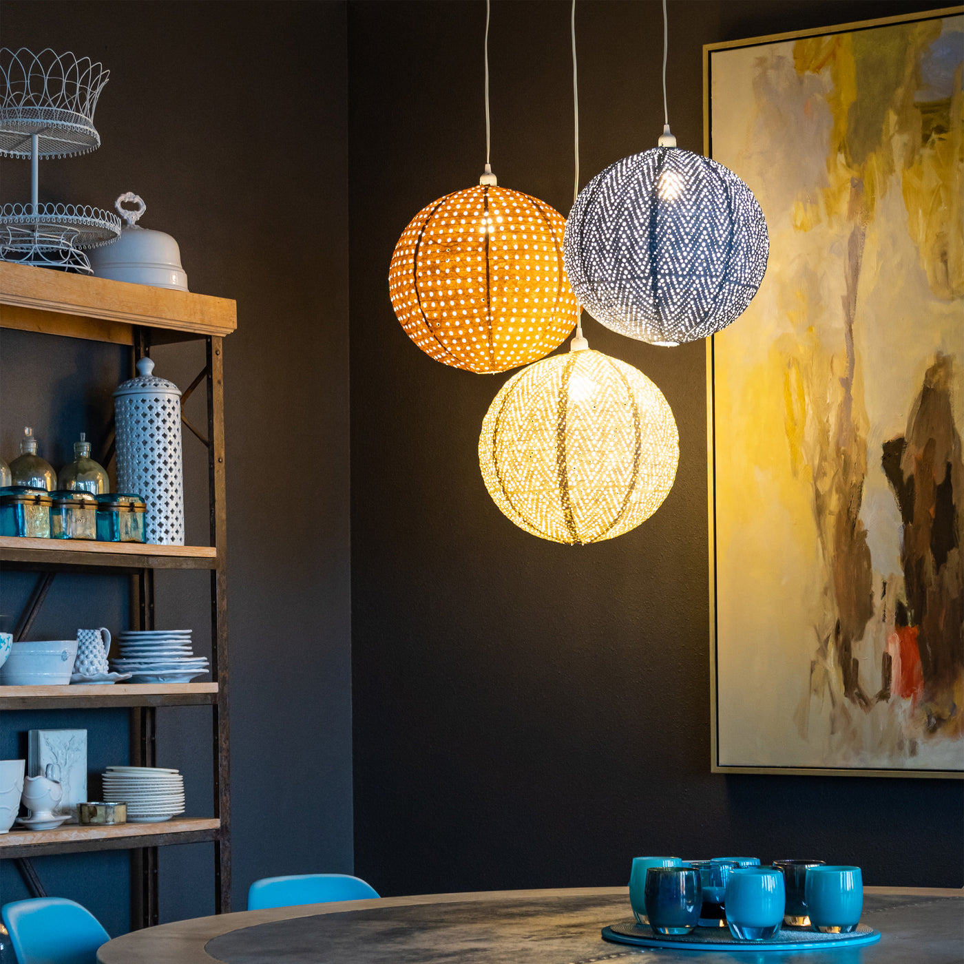 Group of three Stella Nova pendant lamps hanging over a dining table in front of a painting.