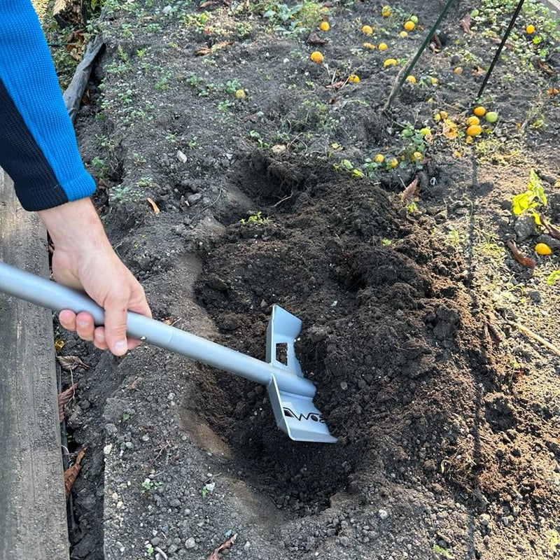 Person using a garden tool to dig into soil in a garden bed